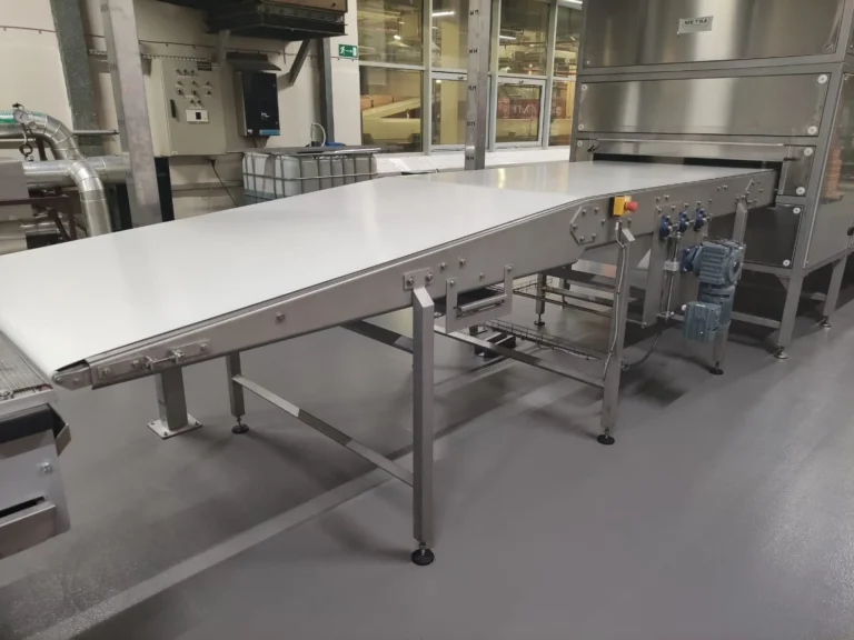 Przenośnik taśmowy z taśmą poliuretanową (PU) wchodzący do tunelu chłodniczego. Konstrukcja łatwozmywalna dedykowana do bezpośredniego kontaktu z żywnością.